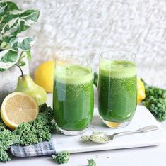 two glasses filled with green liquid next to lemons and broccoli