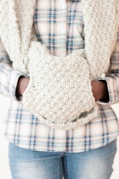 a woman is wearing a crocheted scarf around her neck and holding it in her hands