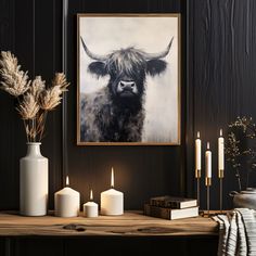 a table topped with candles and vases next to a cow painting on the wall