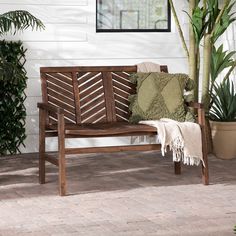 a wooden bench sitting on top of a brick floor next to a potted plant