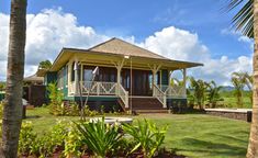 a small house sitting in the middle of a lush green field next to palm trees