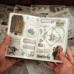 a person holding an open book in their hands with many papers scattered about it on the table