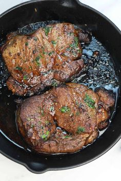 two steaks cooking in a skillet on top of a stove with some seasoning