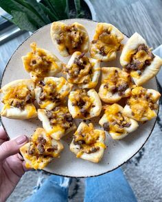 a person holding a plate full of mini pizzas with cheese and meat on them