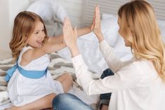 two women sitting on a bed giving each other high fives with their hands in the air