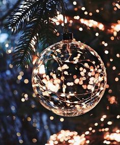 a christmas ornament hanging from a tree with lights in the background and blurry boke