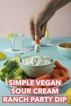 a person dipping dip into a bowl of sour cream surrounded by carrots and broccoli