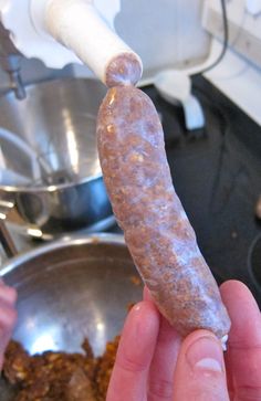 a person holding a sausage in their hand over a frying pan filled with food