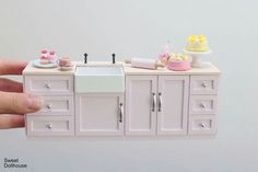 a hand holding a doll house kitchen with sink and cabinets