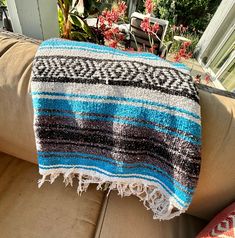 a blue and black blanket sitting on top of a couch next to a flower pot