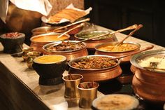 a table filled with lots of different types of food and bowls full of soups