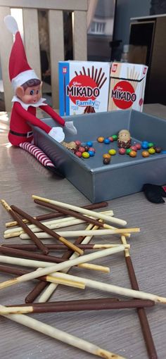 an elf is sitting in front of a box of candy canes and some candies