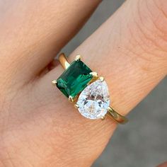 a woman's engagement ring with an oval cut emerald and two pear shaped diamonds