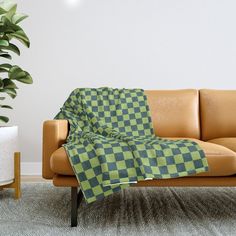 a green and black checkered blanket sitting on top of a couch next to a potted plant