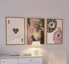 a room with three pictures on the wall and a lamp next to it, in front of a white dresser