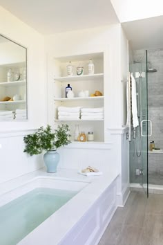 a white bathroom with a tub, sink and shelves filled with towels on the wall