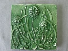 a green ceramic tile with flowers and leaves on it's side, sitting on a gray surface