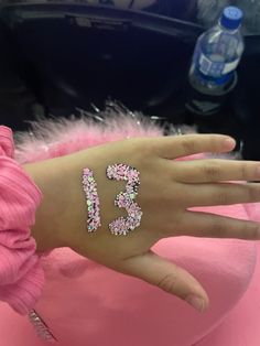 a person's hand with pink and white glitter numbers on their left wrist, next to a bottle of water