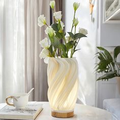 a vase with white flowers sitting on a table next to a book and coffee cup