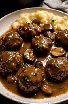 a white plate topped with meatballs covered in gravy and mashed potatoes