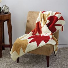 a chair with a blanket on it next to a small table and clock in the corner