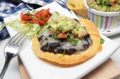 a white plate topped with an enchilada next to a bowl of guacamole