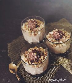 two glasses filled with dessert sitting on top of a table next to spoons and napkin