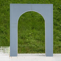 a white bench sitting in front of a blue arch on top of a grass covered field