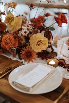 an arrangement of flowers on a table with candles and napkins in front of it