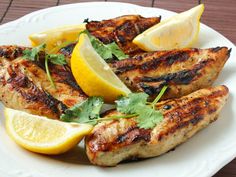 grilled chicken with lemons and cilantro on a white plate, ready to be eaten