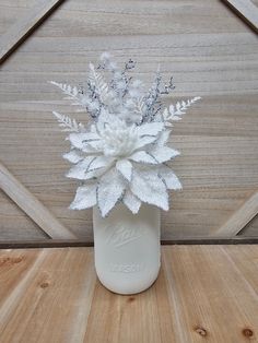 a white vase filled with flowers on top of a wooden table next to a wall