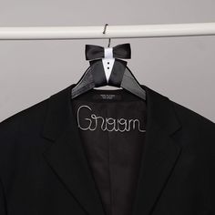 a black suit with a bow tie and the word groom written on it hanging from a white hanger