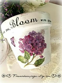 a white flower pot sitting on top of a doily next to purple and green flowers