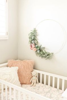 a white crib with a teddy bear and wreath on the wall next to it