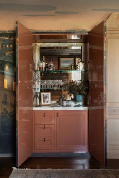 an open cabinet in the corner of a room with paintings on the wall behind it