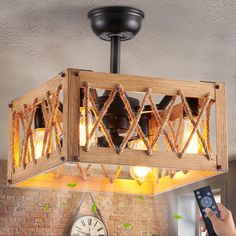 a person holding a remote control in front of a light fixture that is made out of wood