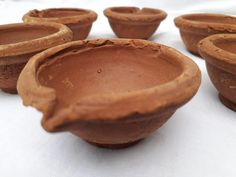 five clay bowls sitting on top of a white cloth covered tablecloth, ready to be used as planters or vases