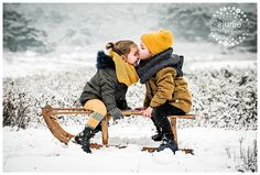 two young children sitting on a sled in the snow, one kissing the other