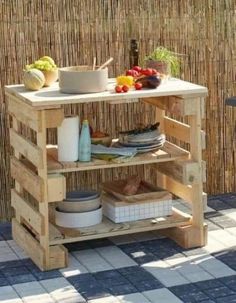 an outdoor table made out of wooden pallets with bowls and plates on it, next to a bamboo fence