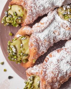 pastries covered in powdered sugar sit on a plate with peas and pistachio