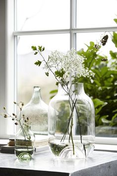 three vases with flowers in them sitting on a window sill next to plants