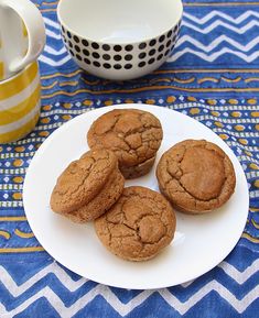 four cookies on a plate next to a cup and saucer with a blue tablecloth