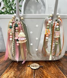 two white purses with tassels on them sitting next to each other in front of a potted plant