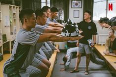 a group of men practicing martial moves in a room with other people standing and sitting around