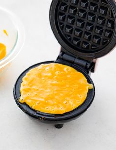 a waffle iron with eggs in it next to a bowl