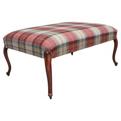 the foot stool is upholstered with plaid fabric and wooden legs, which are attached to