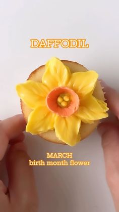 a person holding a small yellow flower on top of a doughnut covered in icing