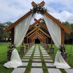 an outdoor wedding ceremony setup with white drapes and flowers on the aisle, surrounded by stone pillars