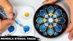 two hands are painting a decorative plate with blue and yellow paint