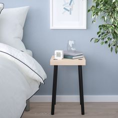 a small table with two books and a glass on it next to a plant in a bedroom